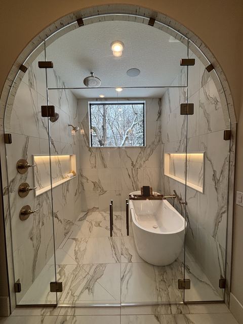 Arched frameless glass wall enclosing a marble bath and shower