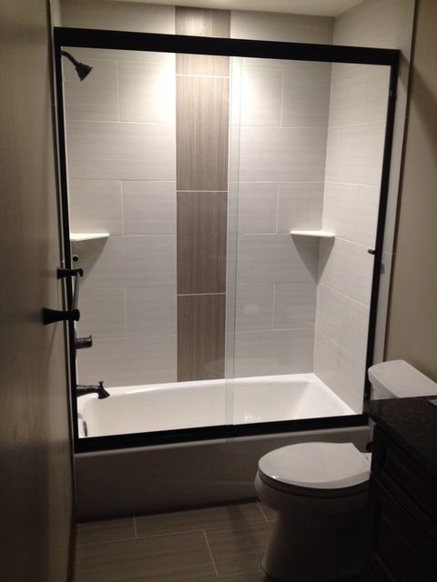 Tub enclosure with black hardware and a vertical tile stripe