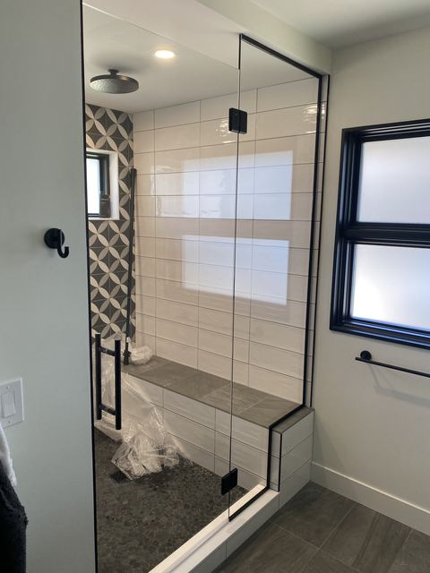 Frameless shower with black hinges beside a window