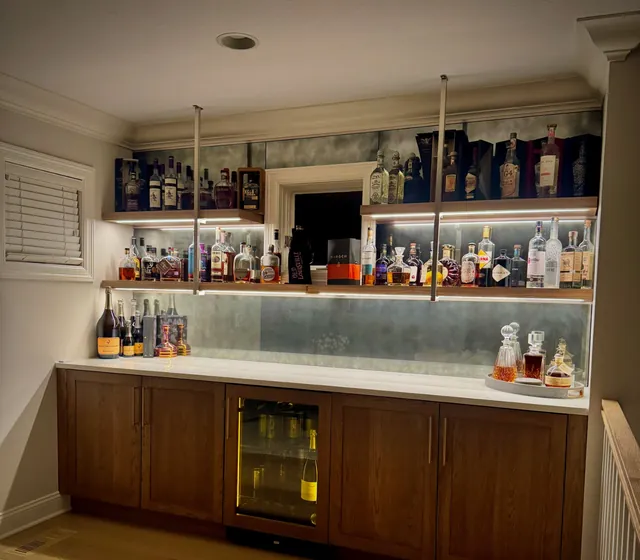 Home bar seen from the side, with the shelf lighting glowing softly in a clouded antique mirror backsplash.