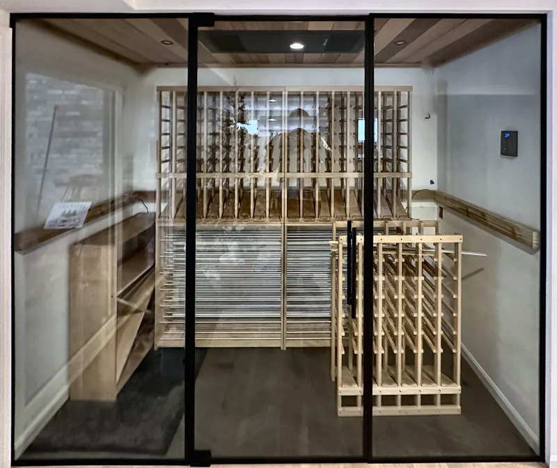 Black-framed glass wall and door into a basement wine room with a cedar ceiling.